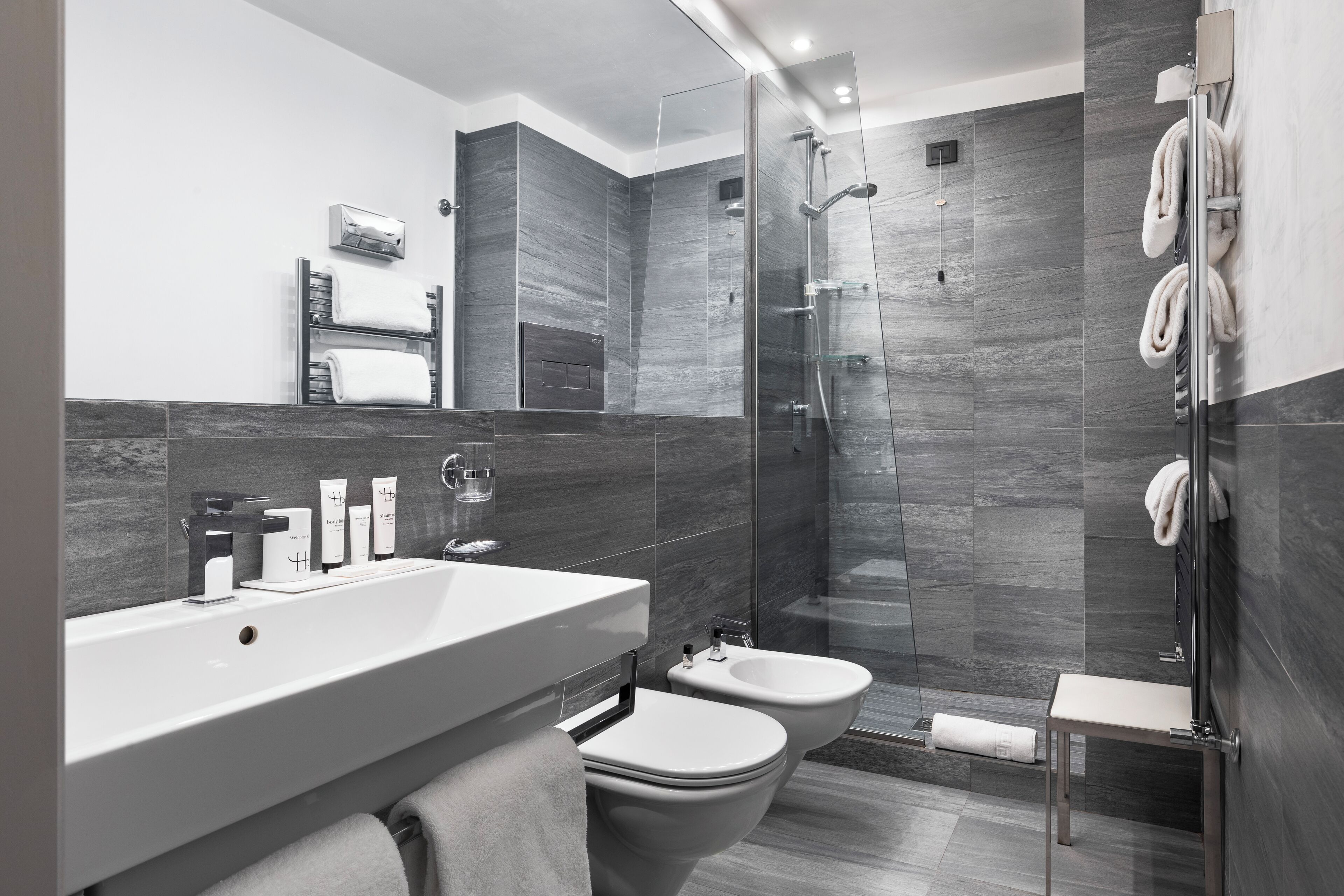 A modern bathroom with a large sink, two toilets, a shower enclosure, and a towel rack.