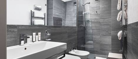 A modern bathroom with a large sink, two toilets, a shower enclosure, and a towel rack.