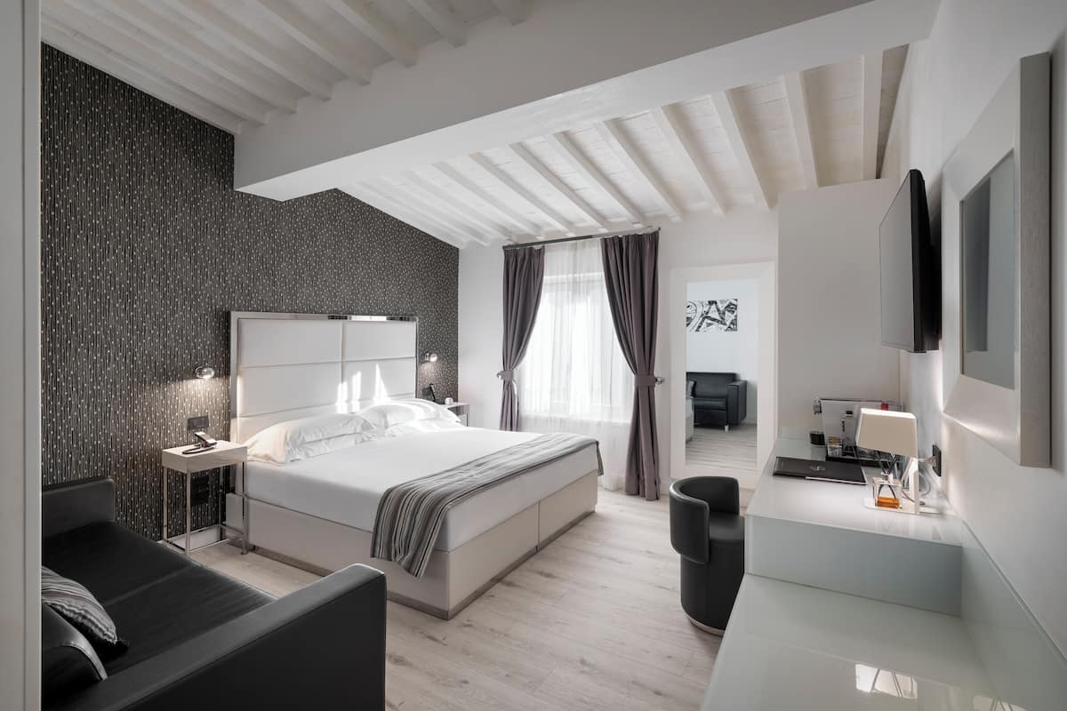 A modern hotel room with a large bed, a desk with a lamp, and a TV mounted on the wall.