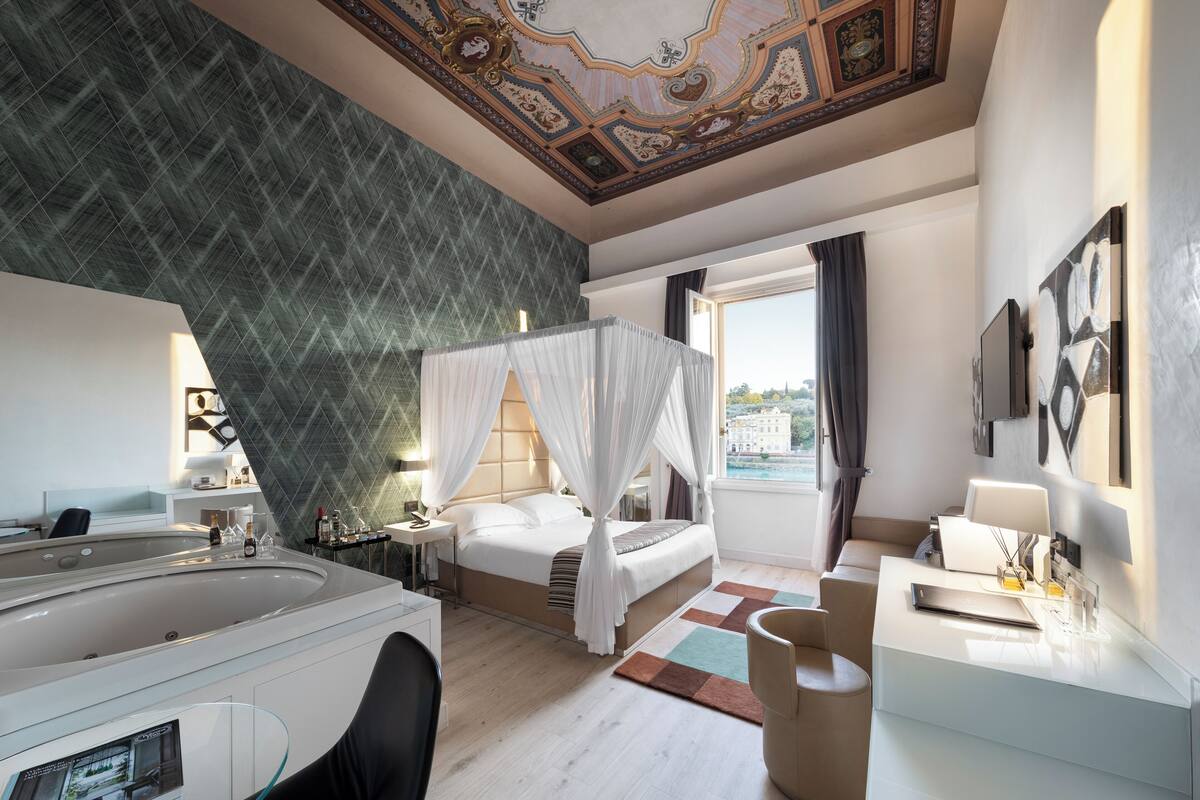A modern hotel room with a large bed, a separate sitting area, a bathtub, and a view of the city.