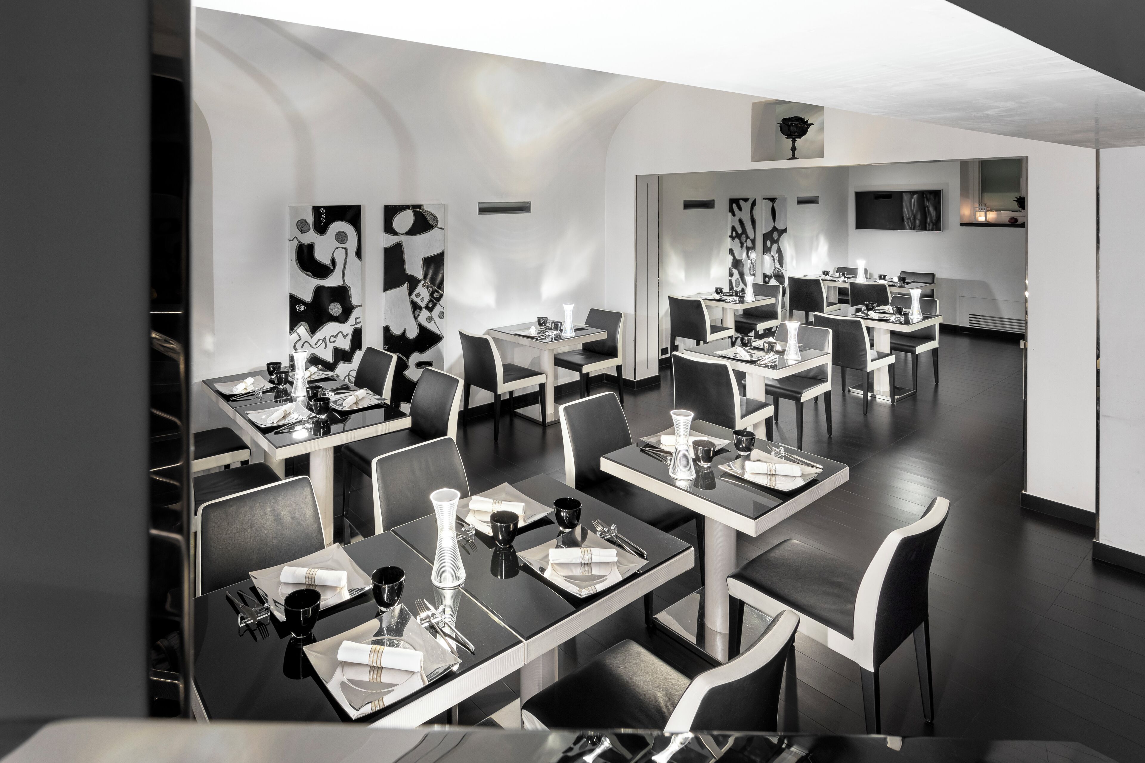 A modern restaurant with black and white decor, featuring multiple dining tables and chairs, and abstract wall art.