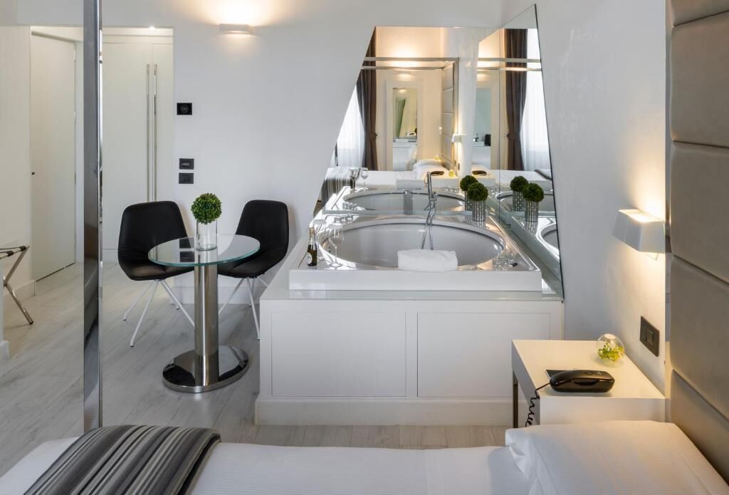 Una habitación de hotel moderna con un escritorio de vidrio, un espejo redondo, una bañera y una cama.