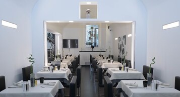 En moderne restaurant med flere spiseborde, stole og et centralt placeret fjernsyn.