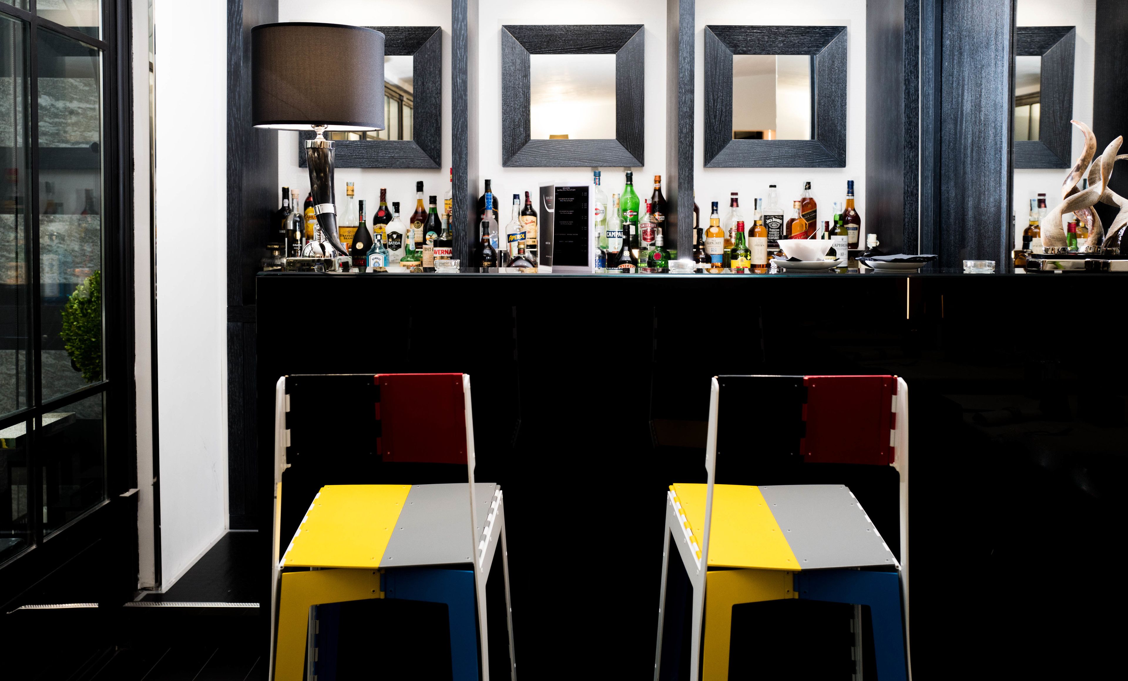 Eine Bar mit einer Auswahl an Spirituosenflaschen, einem Spiegel und zwei stuhlähnlichen Sitzgelegenheiten mit farbigem Muster.