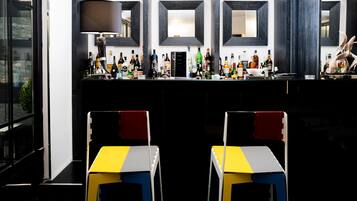 Eine Bar mit einer Auswahl an Spirituosenflaschen, einem Spiegel und zwei stuhlähnlichen Sitzgelegenheiten mit farbigem Muster.