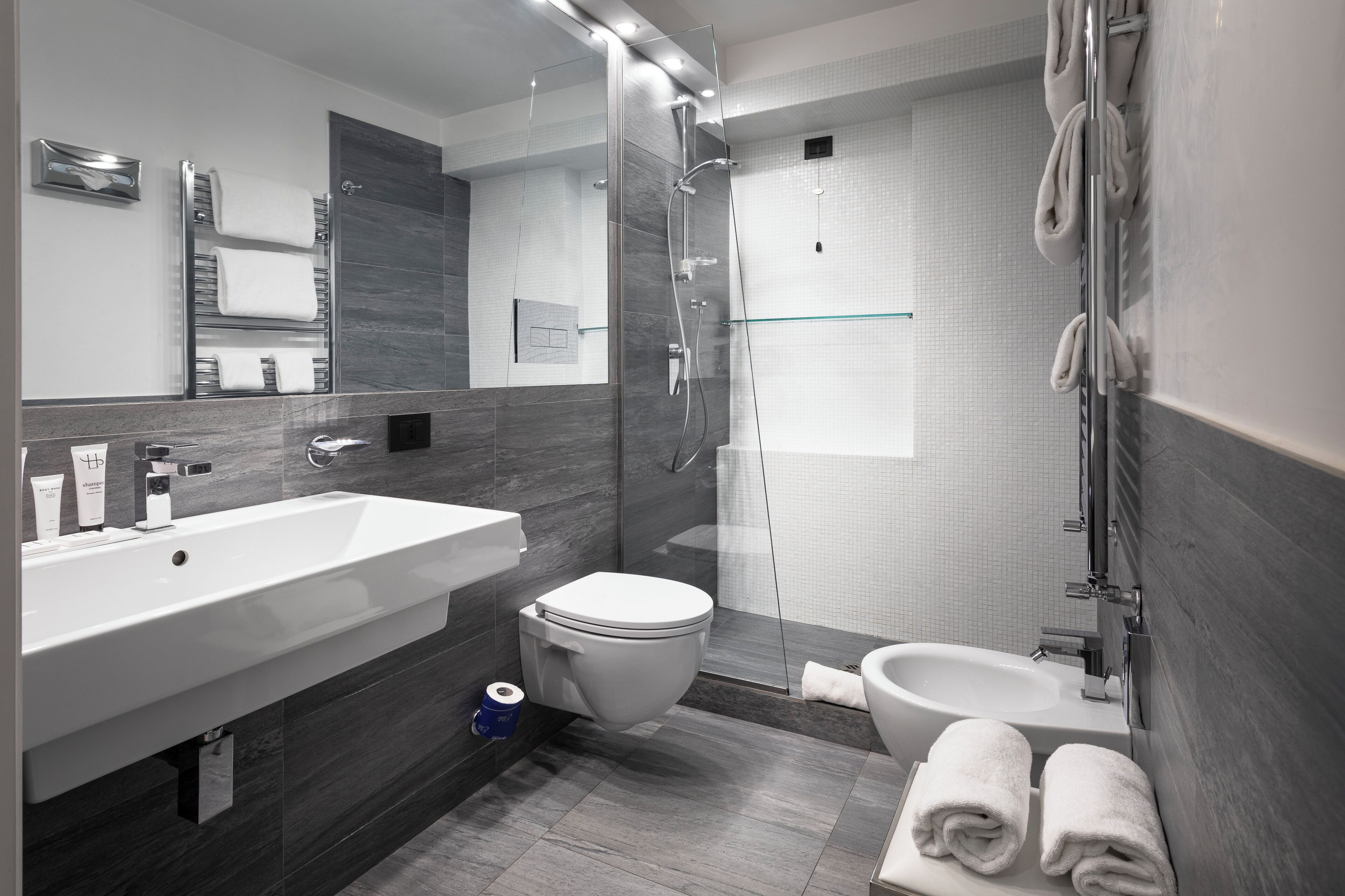 Un baño moderno con un lavabo grande, inodoro, bidé, cabina de ducha de cristal y toallas ordenadas.