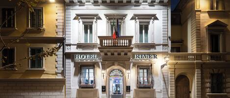 A historic hotel facade with a grand entrance, columns, and a balcony with flags.