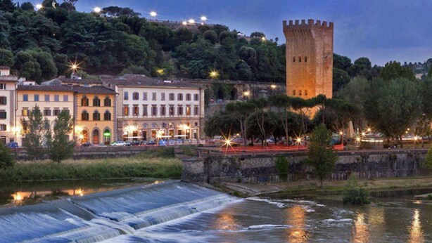 A historic town with a prominent tower, a river with a water mill, and buildings with illuminated windows. - LHP Hotel River & SPA (Florence)