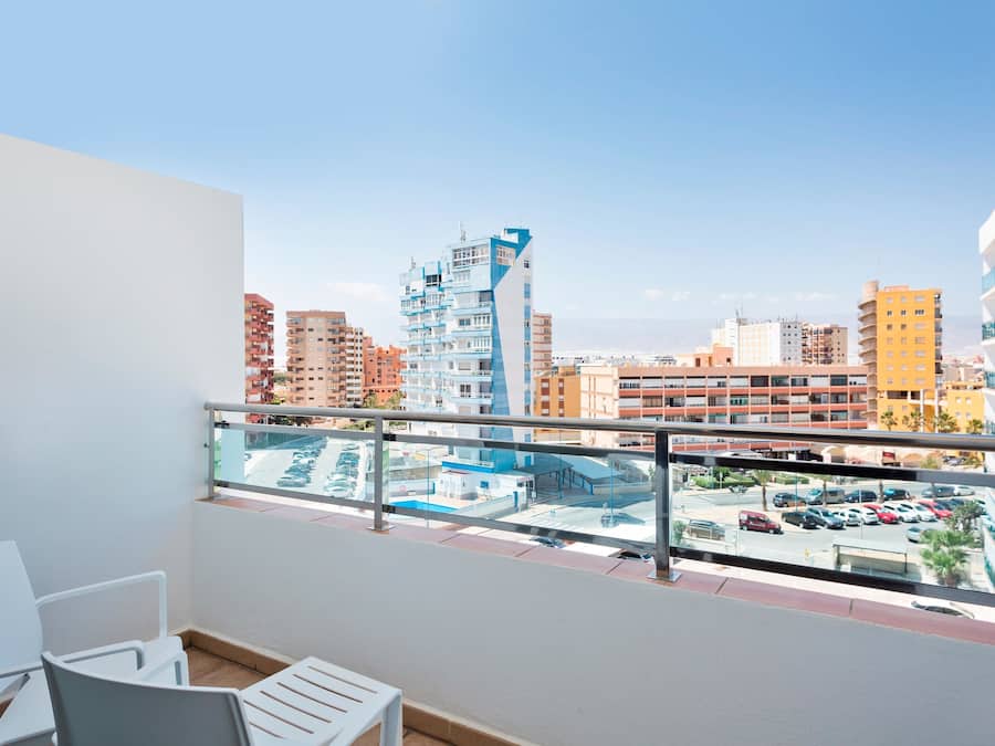 A balcony with a view of a cityscape, including modern buildings and a parking area.