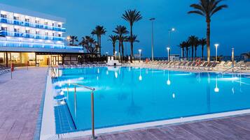 A large indoor swimming pool with lounge chairs and palm trees, surrounded by a modern hotel building.