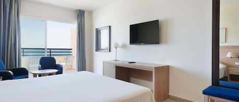 Habitación de hotel con cama, escritorio, silla, televisión y balcón con cortinas.