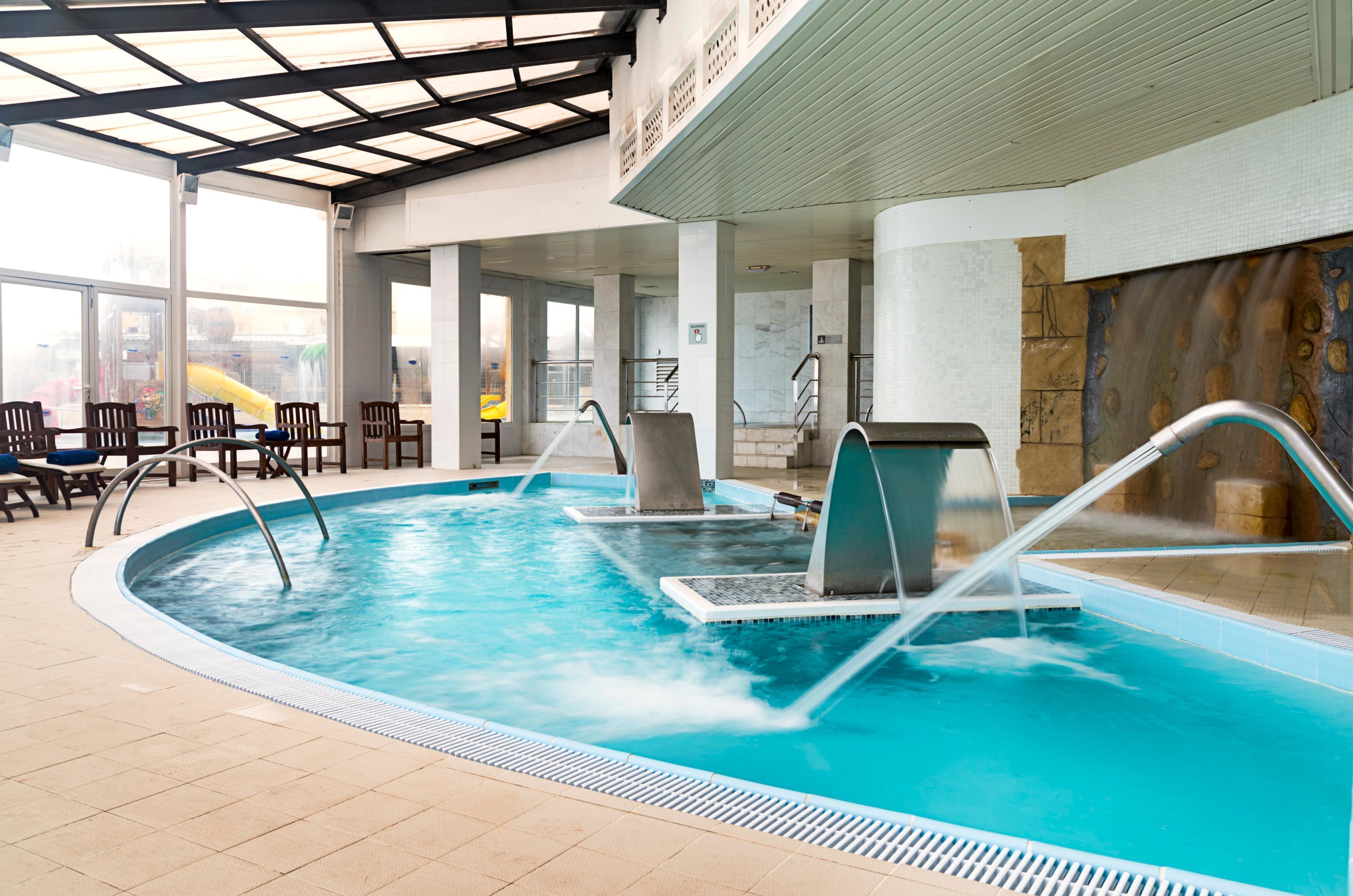 Una piscina interior con múltiples carriles, techo cubierto y pared de piedra.