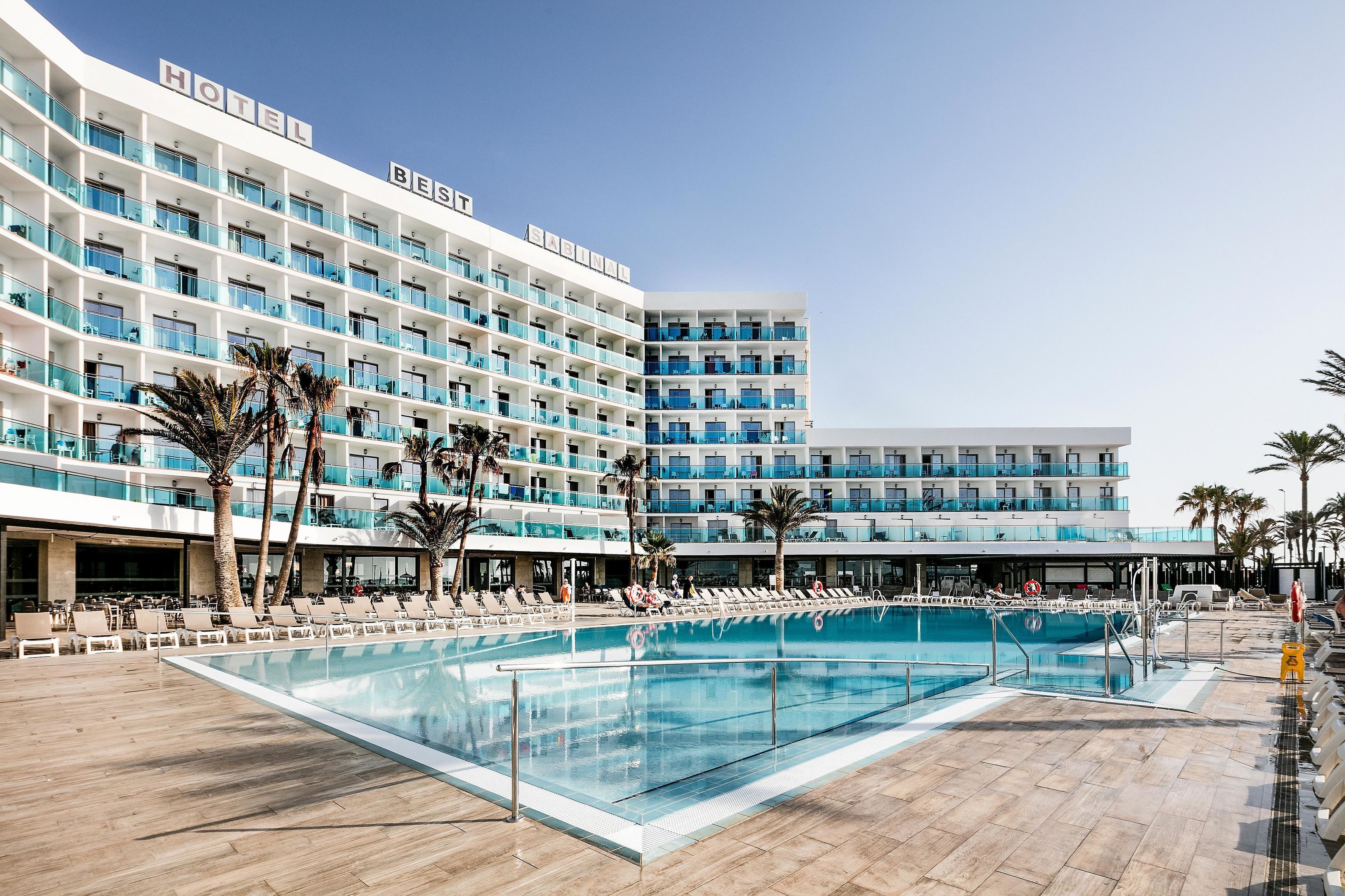 A hotel with multiple balconies, a swimming pool, and palm trees.