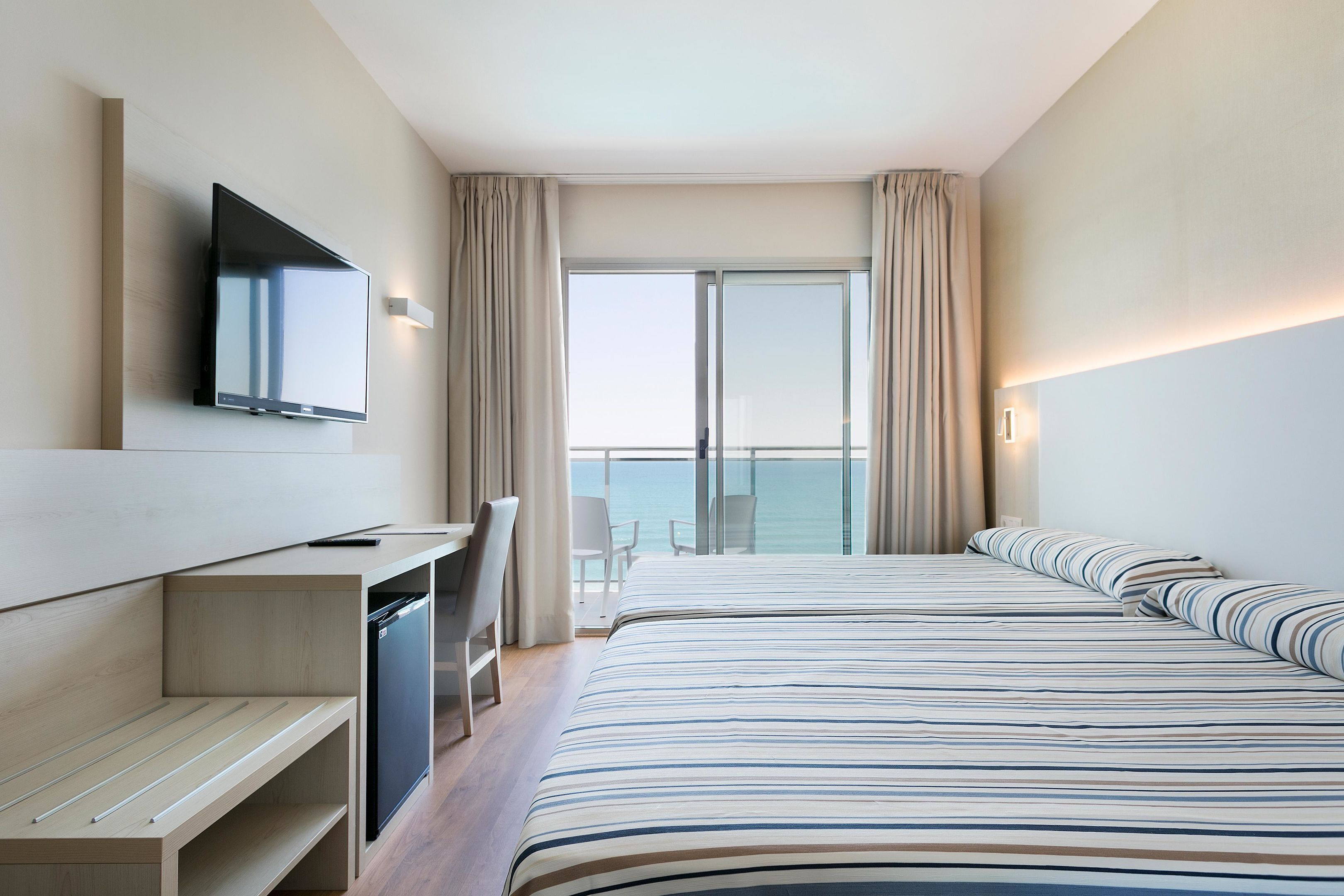 Ein modernes Hotelzimmer mit einem großen Bett, einem Schreibtisch, einem Flachbildfernseher und einem Balkon mit Meerblick.