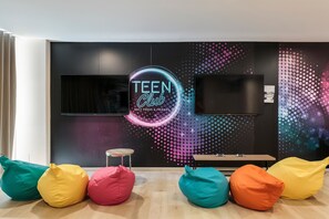 A modern living room with a neon sign reading "TEEN Club" and a flat-screen TV mounted on the wall. - Hotel Best Sabinal (Roquetas de Mar)