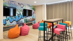 Una sala de estar moderna con un televisor de pantalla plana montado en la pared, coloridos pufs y una mesa de comedor de madera con taburetes de bar.