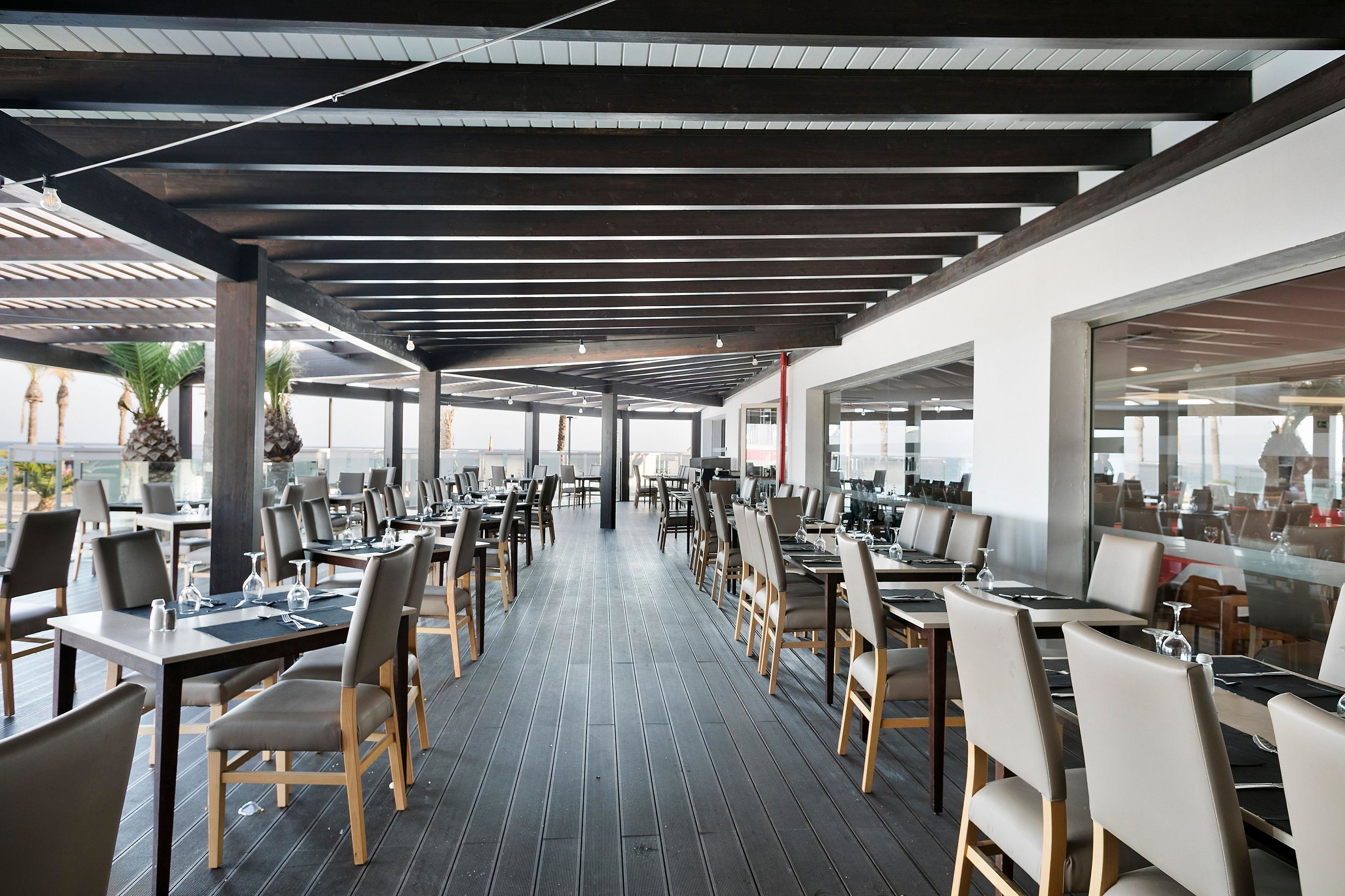 Un vaste espace extérieur aménagé pour les repas, avec plusieurs tables et chaises, un plancher en bois et une structure de plafond moderne.