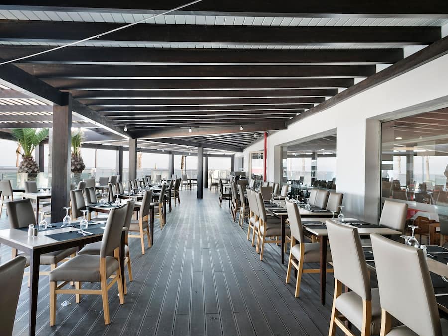 Un amplio espacio exterior para comer con varias mesas y sillas, piso de madera y una estructura de techo moderna.