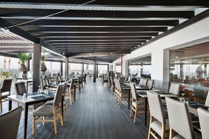 A spacious outdoor dining area with multiple tables and chairs, a wooden floor, and a modern ceiling structure.