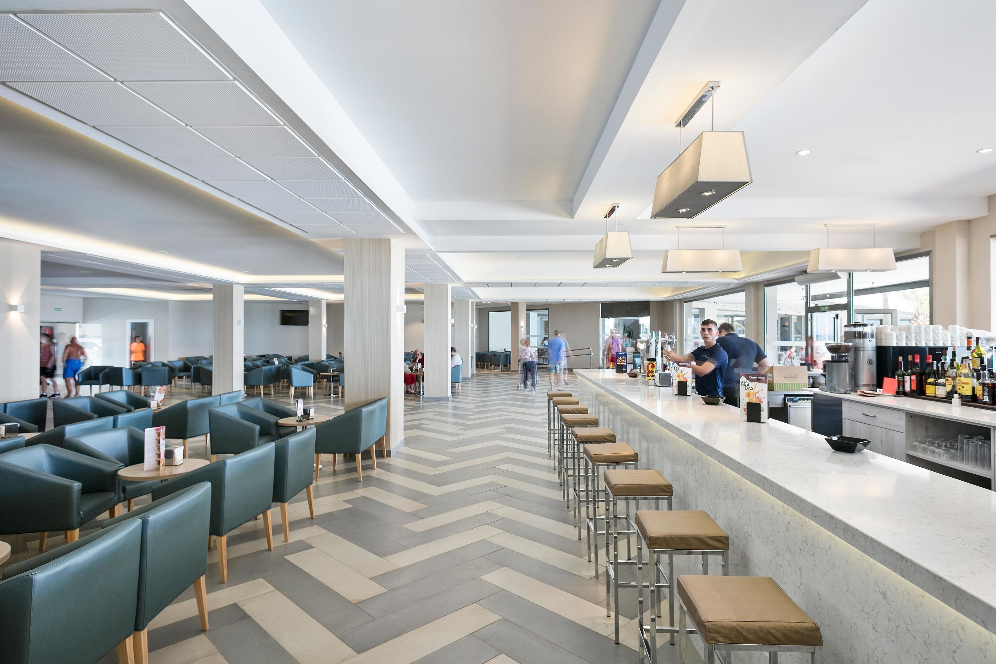 Un restaurant moderne doté d’un long comptoir, de tabourets de bar et d’un espace bar avec un présentoir à bouteilles.