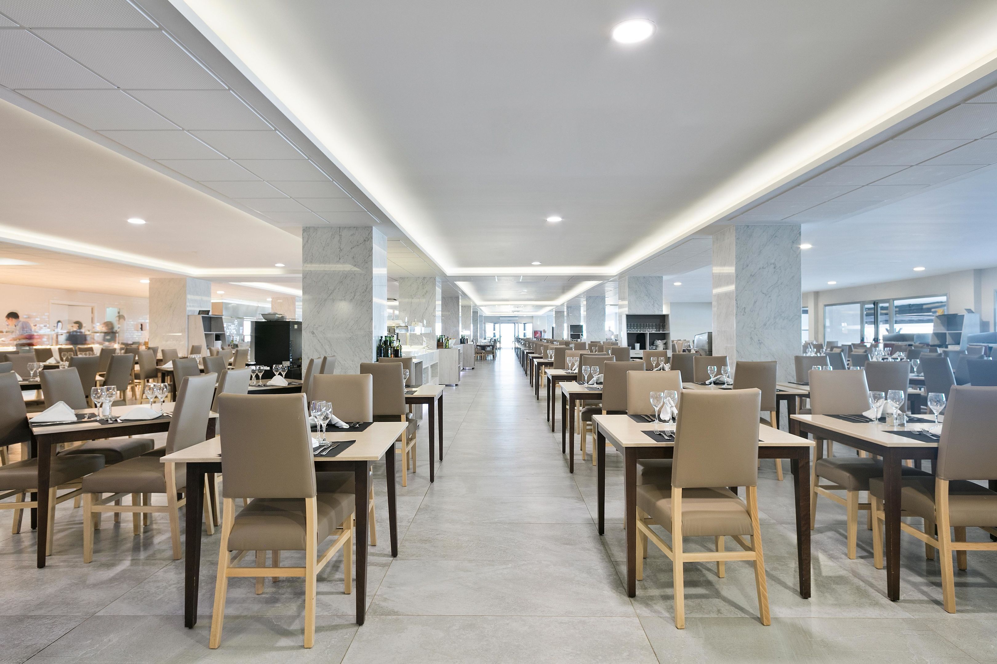 Un comedor amplio con varias mesas y sillas, suelo impecable y diseño moderno de techo.
