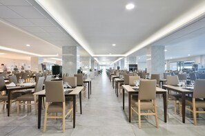 Un comedor amplio con varias mesas y sillas, suelo impecable y diseño moderno de techo.