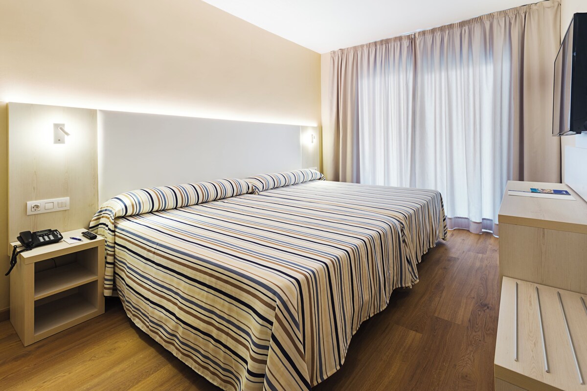 Habitación de hotel con una cama grande, mesitas de noche, un escritorio y un televisor.