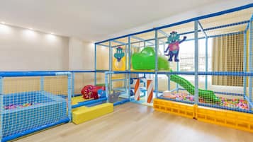 Zona de juegos con tobogán, red de escalada y estructuras acolchadas.