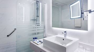 Un baño moderno con cabina de ducha de vidrio, un lavabo blanco y un espejo grande.