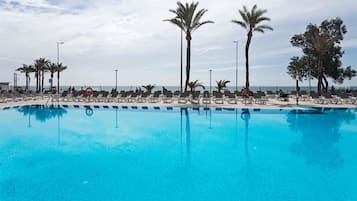 Zona junto a la piscina con sillas de descanso y palmeras, con vista a una extensión de agua.