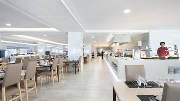 Een modern restaurant met een lange toonbank, meerdere tafels en een open keuken.