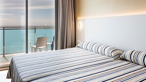 Habitación de hotel con una cama grande, vista al mar y un balcón con una silla.