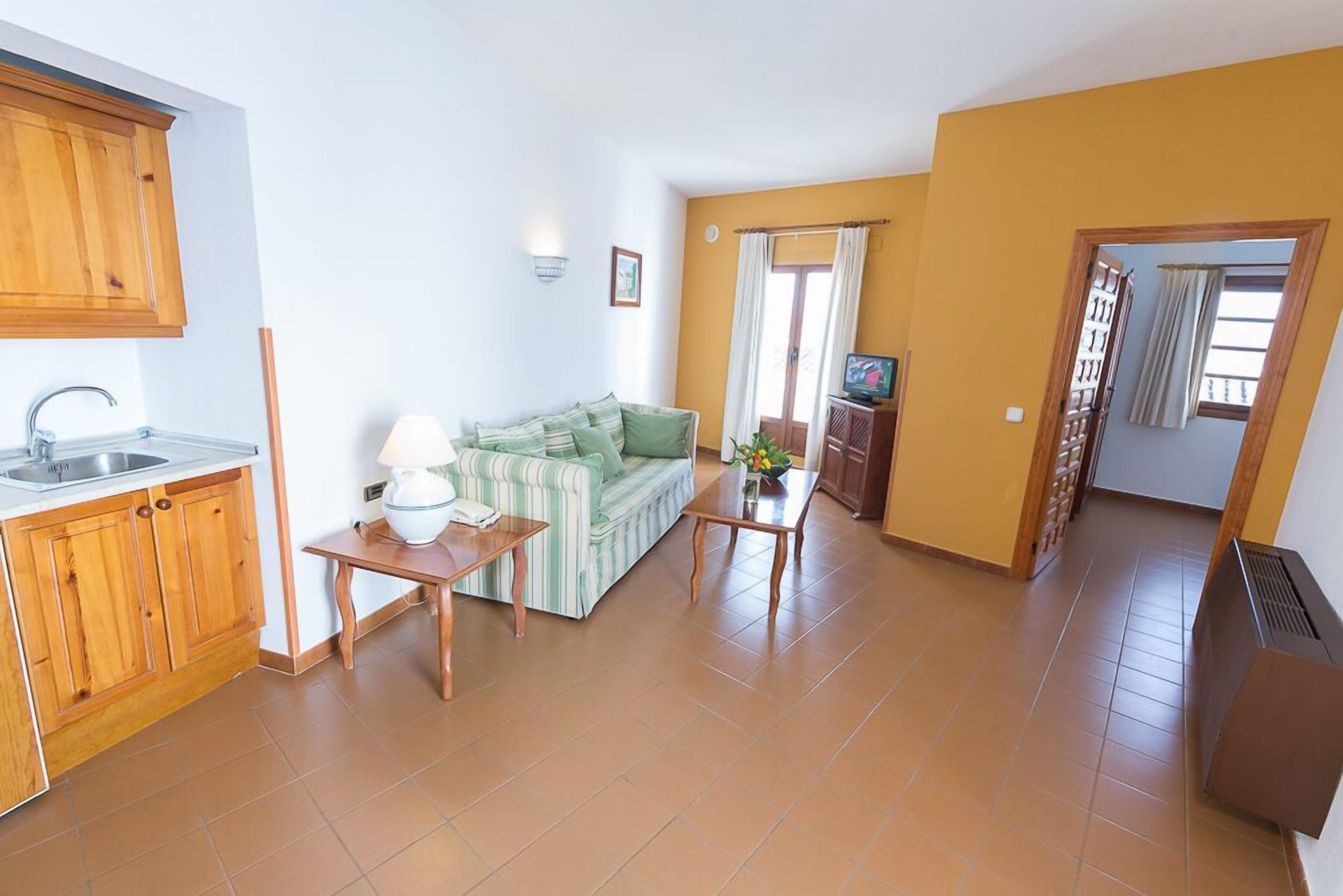 A compact living space with a kitchenette, a sofa, a small table, and a TV.