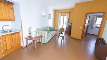 A compact living space with a kitchenette, a sofa, a small table, and a TV.
