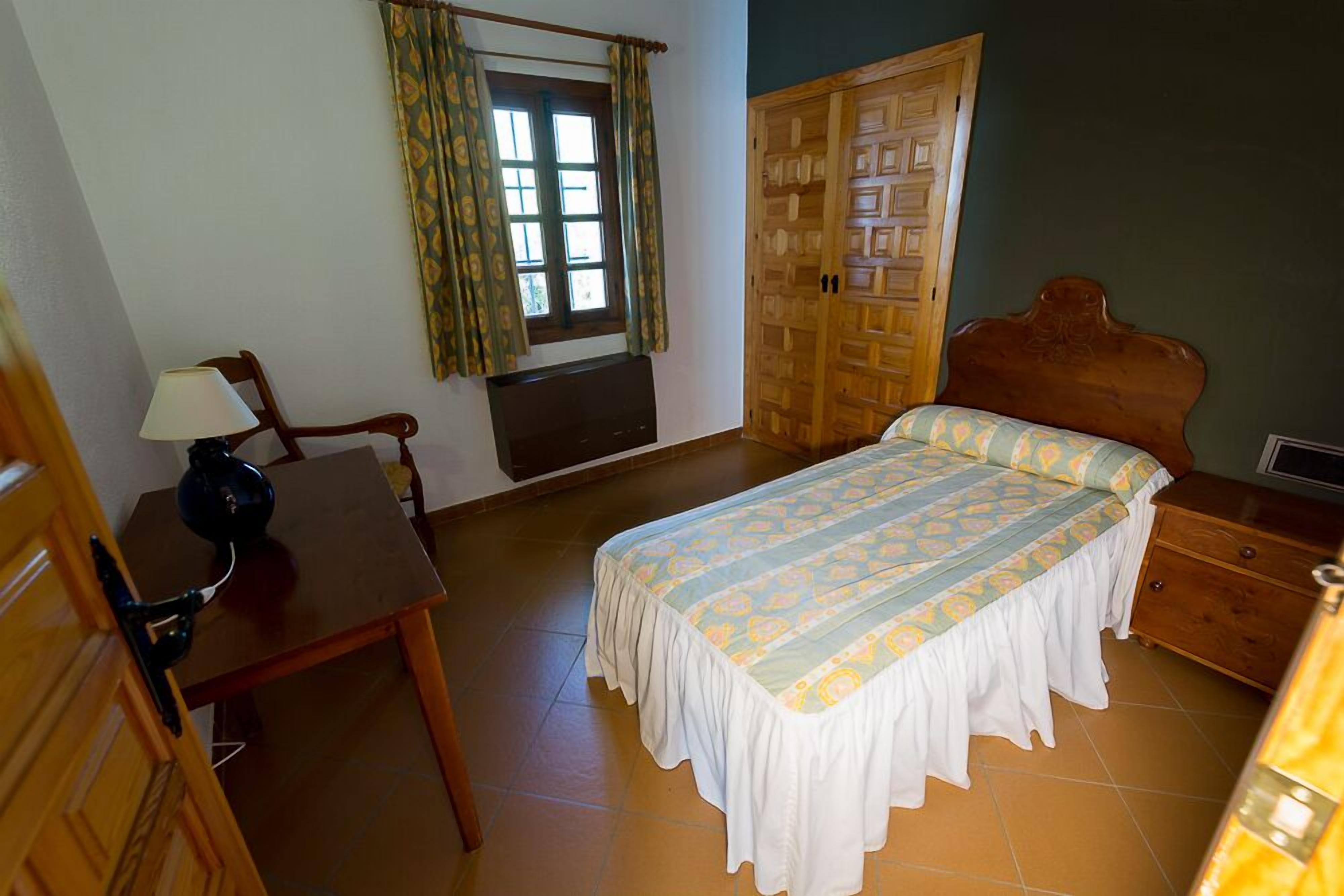 A bedroom with a bed, a desk, a chair, a wardrobe, and a window with curtains.