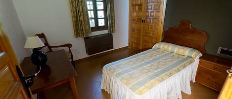 Une chambre à coucher avec un lit, un bureau, une chaise, une armoire et une fenêtre avec des rideaux.