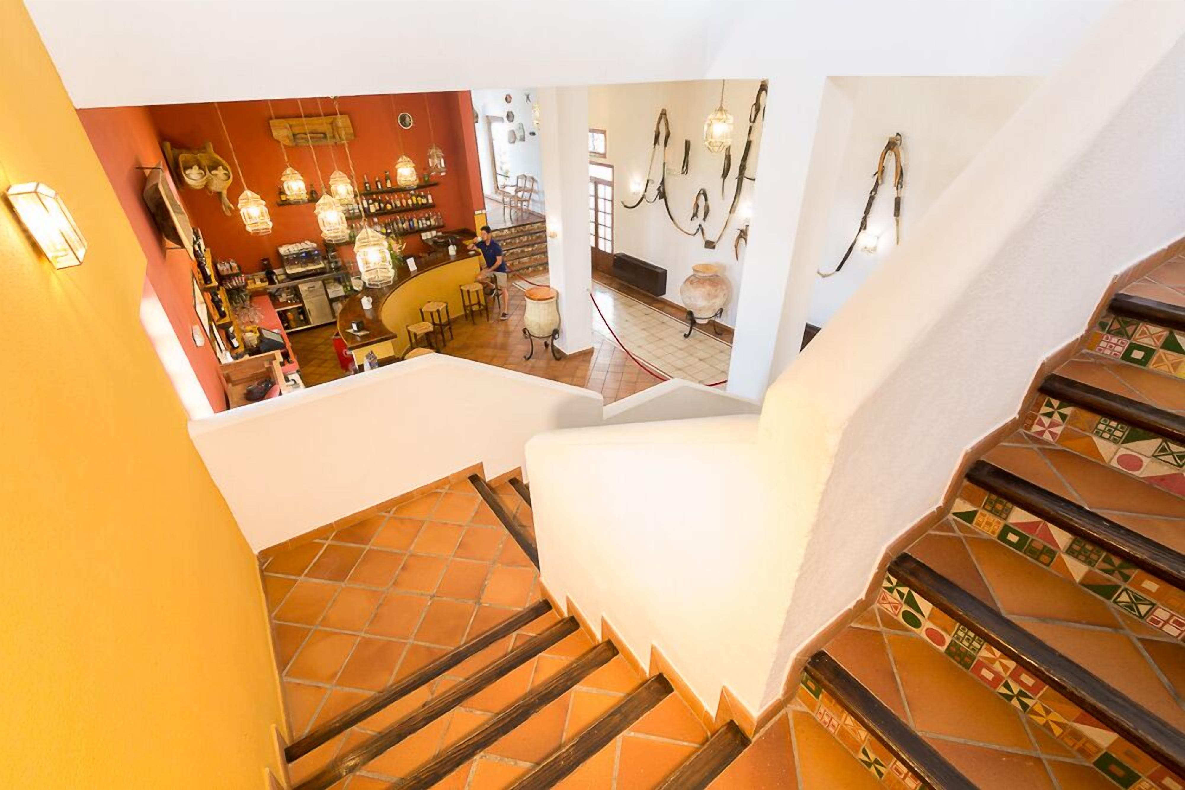 Una escalera con una silla blanca, una zona de bar con luces colgantes y un suelo de baldosas.