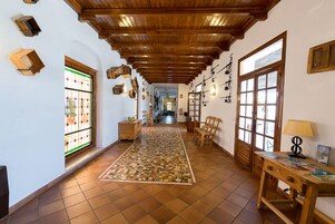 Un pasillo con alfombra estampada, vigas de madera en el techo y una mesa de madera con una lámpara.