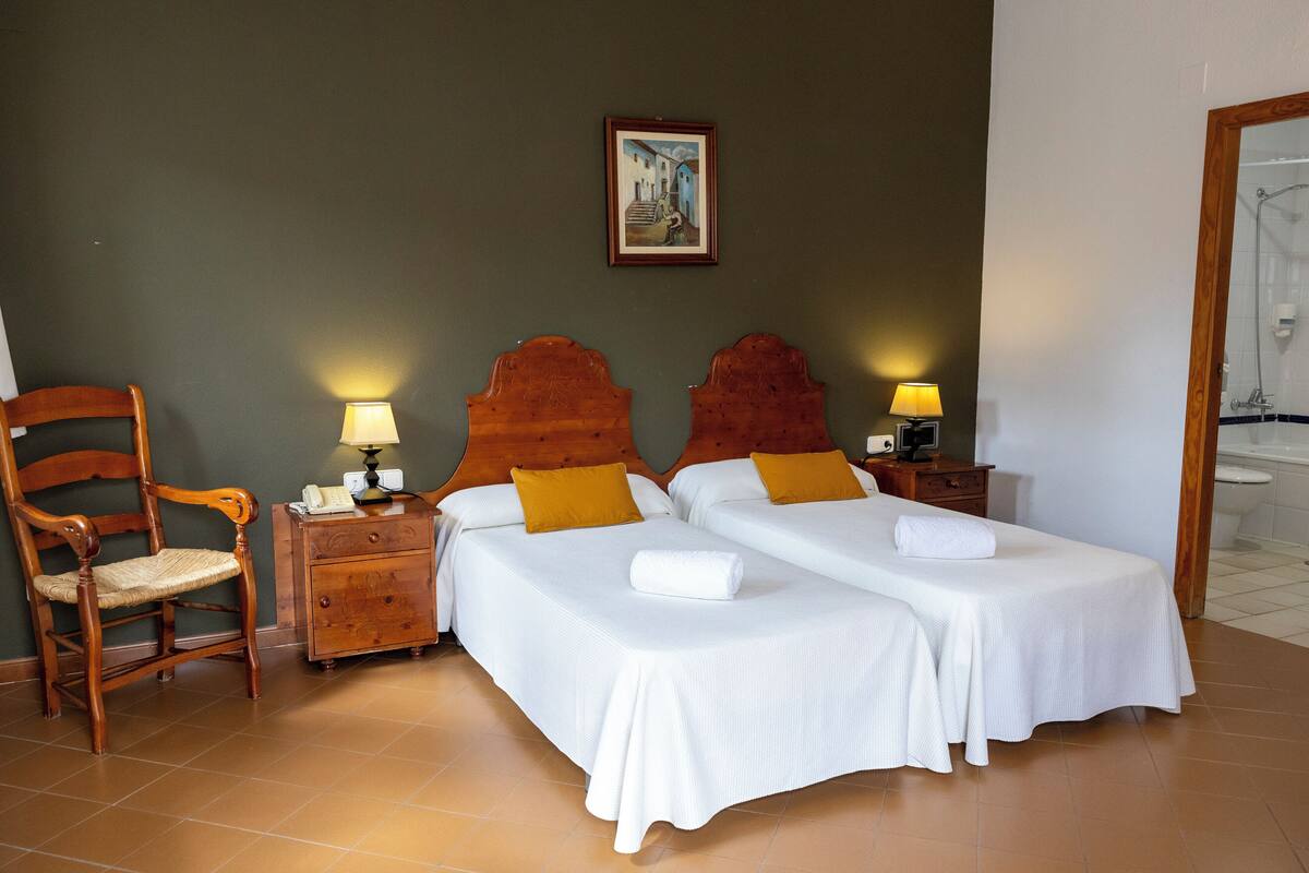 A hotel room with two beds, a wooden chair, a nightstand with a lamp, and a painting on the wall.