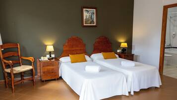 A hotel room with two beds, a wooden chair, a nightstand with a lamp, and a painting on the wall.