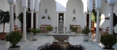 A courtyard with white columns, potted plants, and a central fountain.