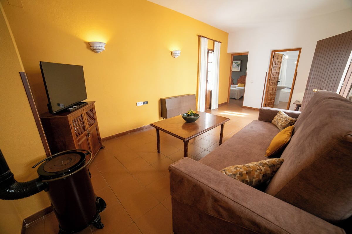 A living room with a sofa, a coffee table, a TV on a cabinet, and a trash can.