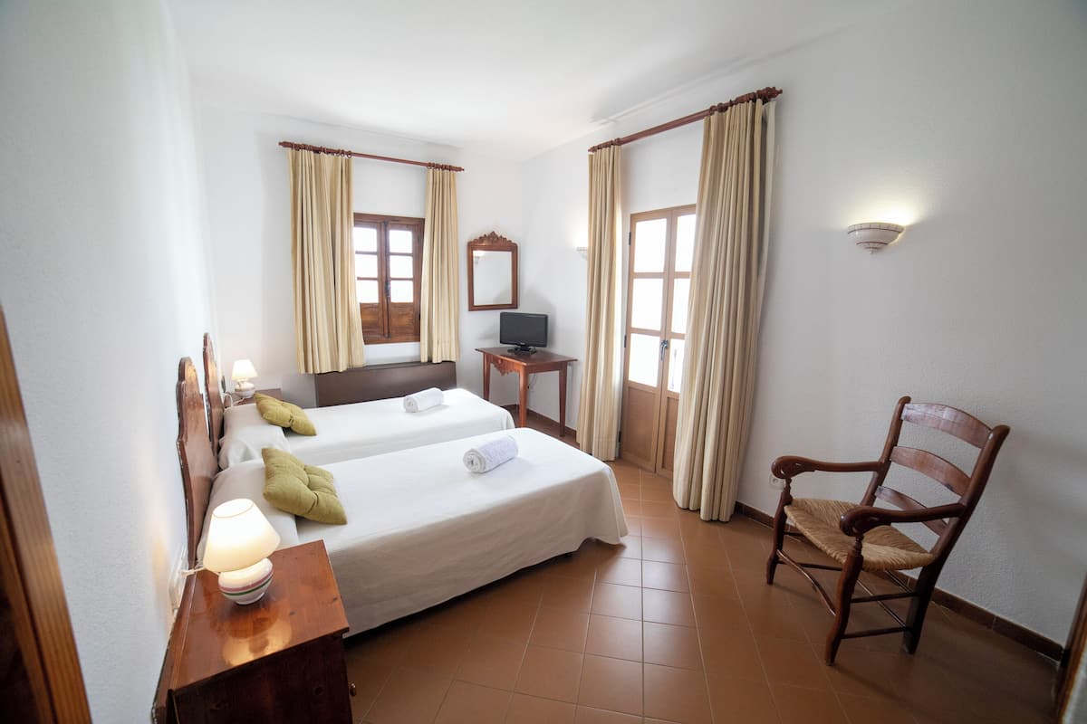A hotel room with two beds, a desk with a lamp, a chair, a TV, and curtains.