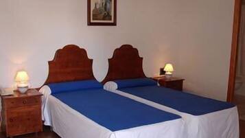 A double room with two beds, each with a blue bedspread and white sheets, wooden headboards, bedside tables with lamps, and a framed picture on the wall.