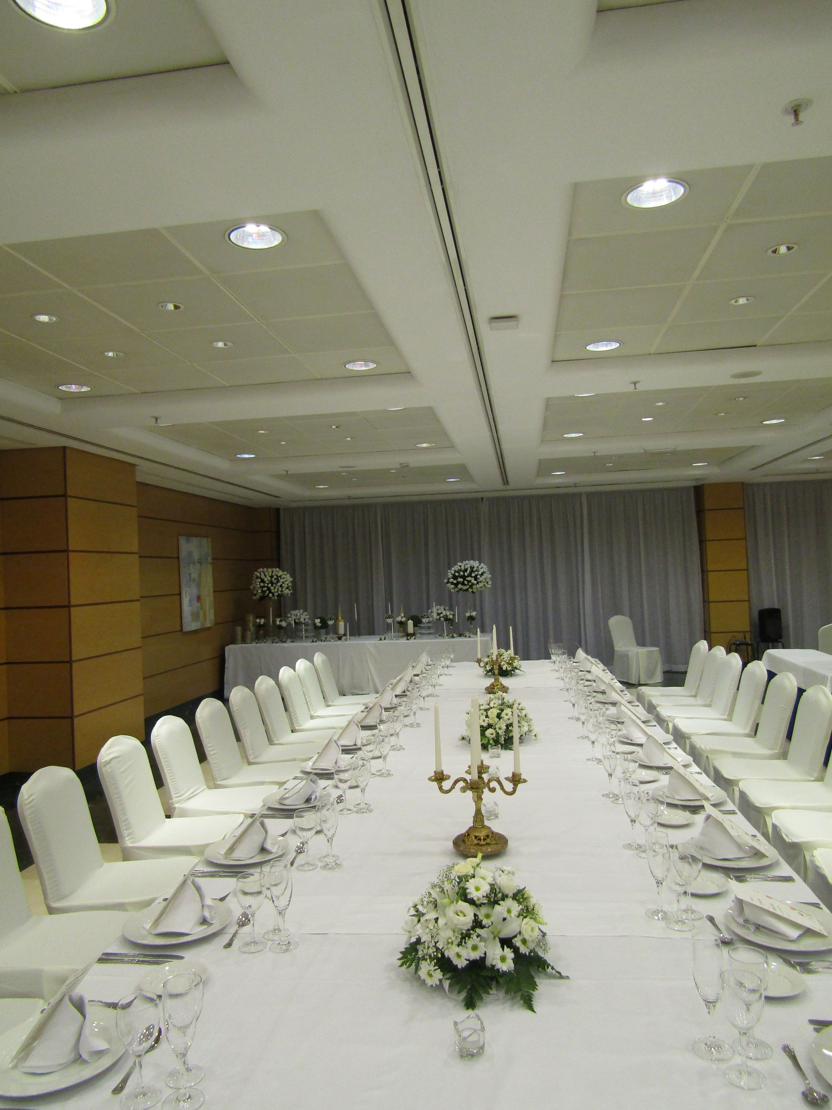 A banquet hall with a long table set for a formal event, featuring white chairs and table settings.