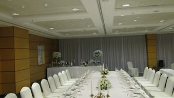 A banquet hall with a long table set for a formal event, featuring white chairs and table settings.