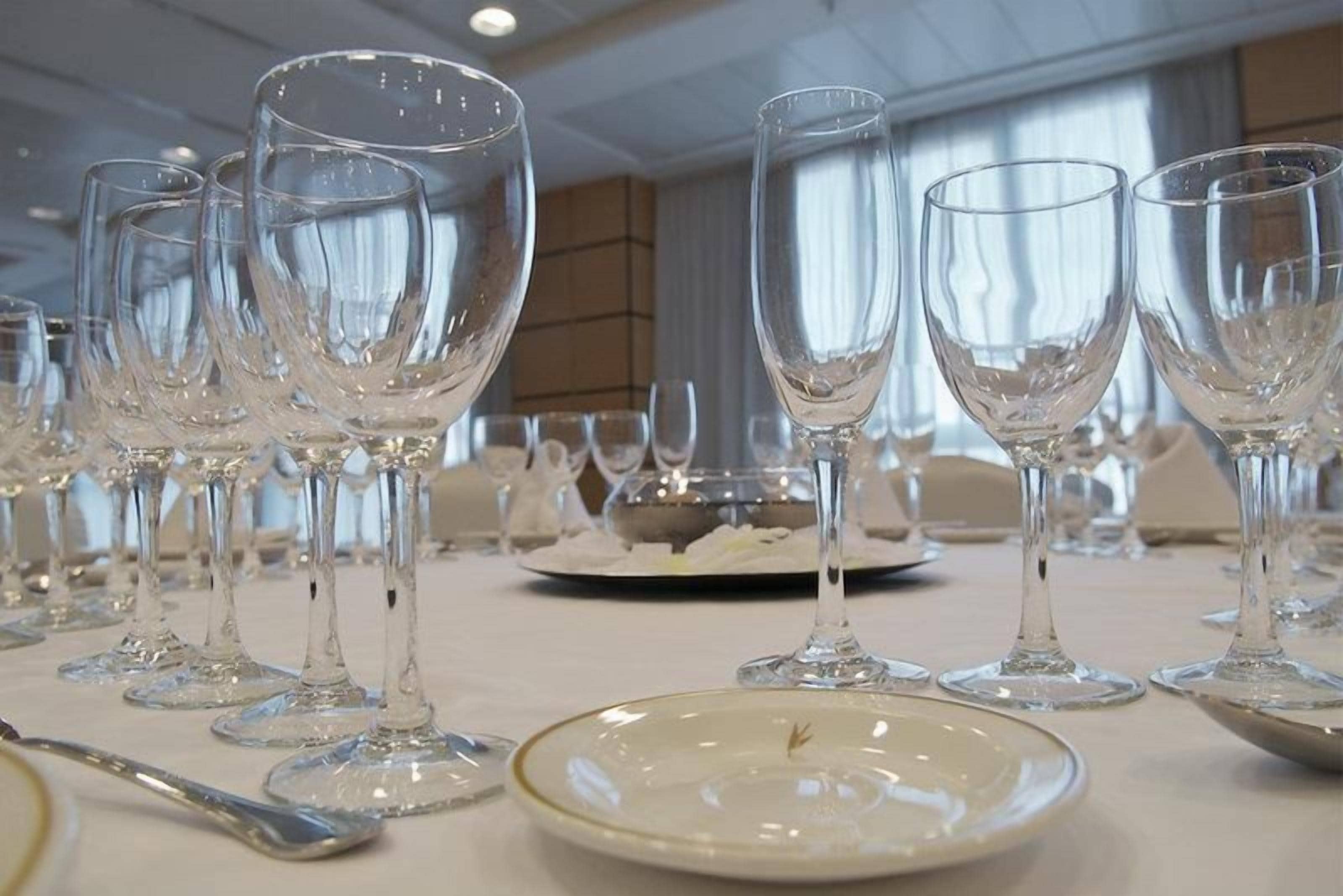 Una mesa dispuesta con varias copas de vino y platos, indicando una disposición formal para cenar.