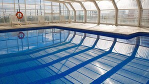 An indoor swimming pool with clear glass walls, a tiled floor, and several lounge chairs. - Hotel Albufera (Alfafar)