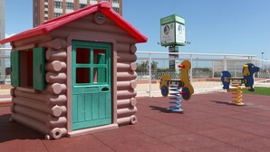 A children's play area with a log cabin structure, swings, and a spring-mounted toy. - Hotel Albufera (Alfafar)