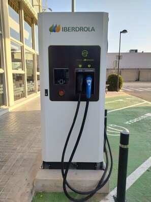 Eine Ladestation für Elektrofahrzeuge mit dem Schriftzug "IBERDROLA" auf einem Parkplatz.